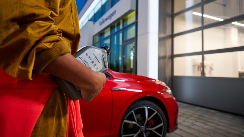 Inquadratura di una persona reggere in mano una bottiglia di olio per motore LongLife III FE e sullo sfondo un veicolo Volkswagen. 