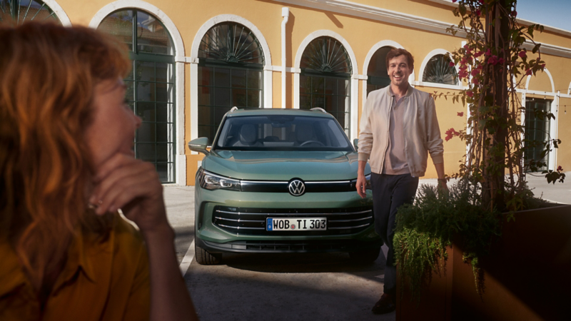 Un ragazzo si allontana sorridente dalla sua Tiguan verde per dirigersi verso una ragazza che lo attende.